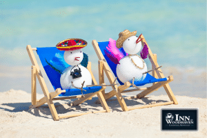 Two white arts and crafts birds made from styrofoam, beads, and colorful feathers sit in blue beach chairs on the sand.