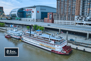 Old steamship called the Belle of Louisville on the Ohio River, in front of a high rise and stadium.