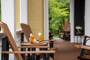 A porch view with two adirondack chairs and two glasses of iced tea with lemon slices on a table between them.